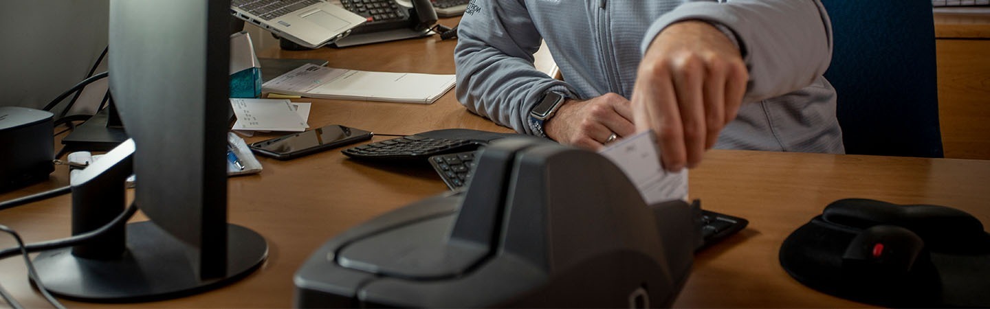 Man sitting at a desk, scanning a check into a remote deposit check scanner.